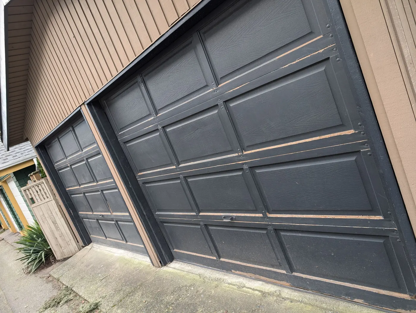 Weathered black double garage door with peeling paint on a Vancouver home, ready for refinishing by Renaissance Painting.