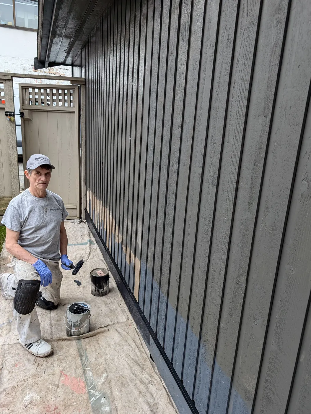 Renaissance Painting crew member rolling dark stain onto a vertical wood fence panel in Vancouver, BC.