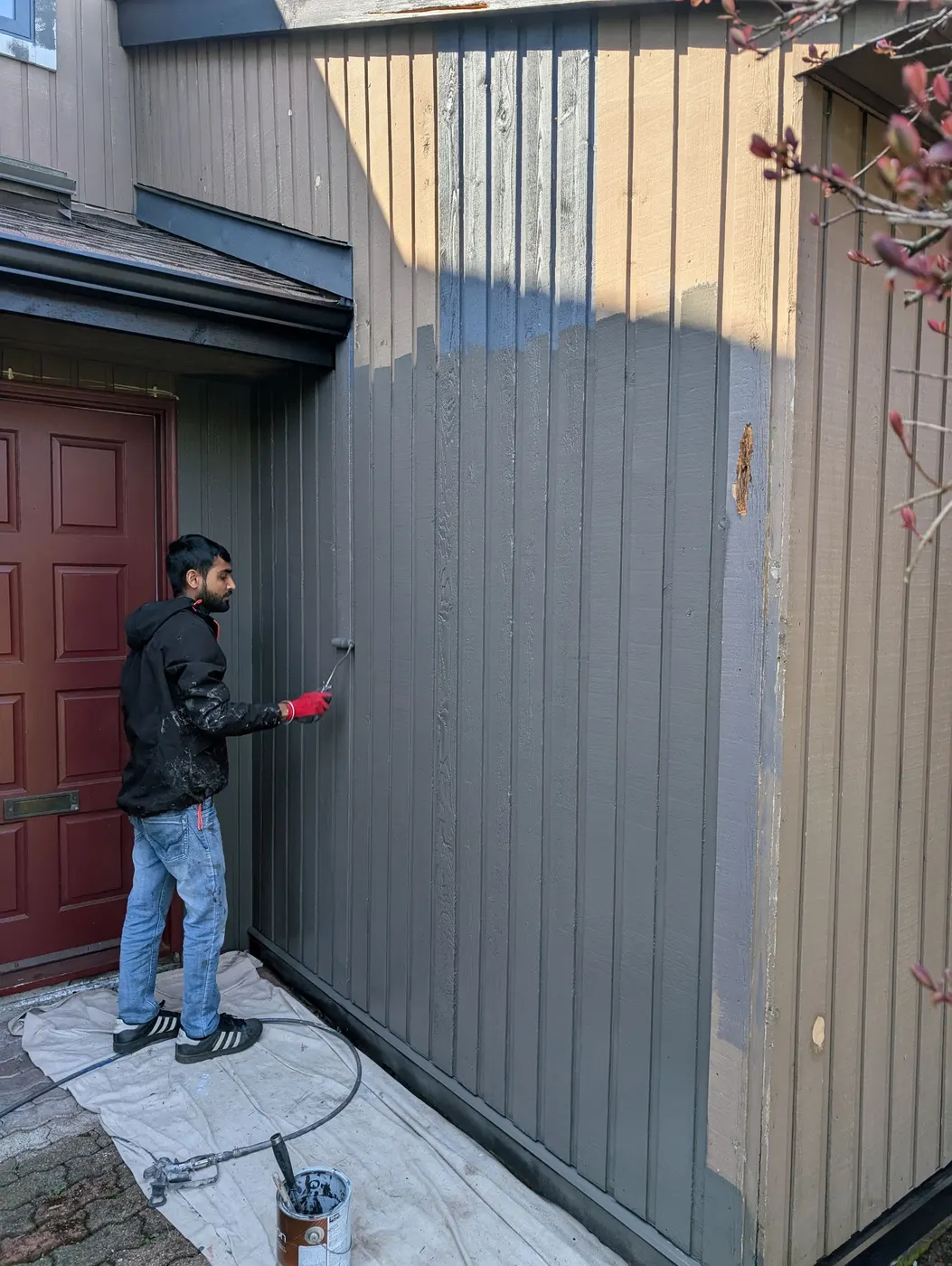 Renaissance Painting crew member rolling fresh gray paint onto vertical wood siding beside a maroon front door in Vancouver.