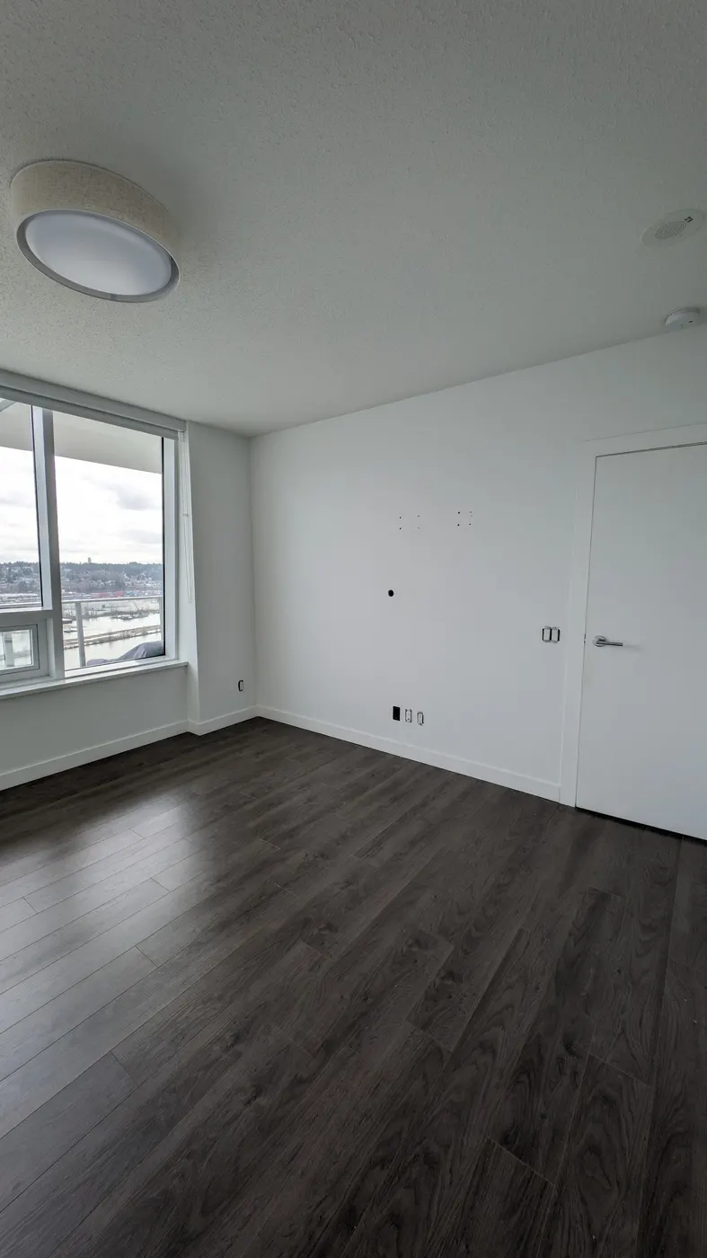 Freshly installed white baseboard trim along a Vancouver condo bedroom corner with dark laminate flooring.