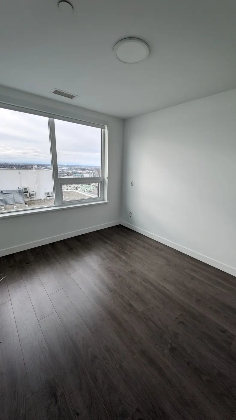 New white baseboard trim installed beneath a large window in a Vancouver condo bedroom.