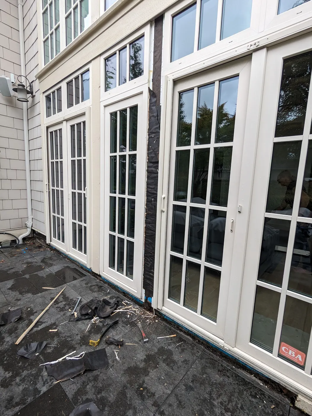 Carpenter repairing weatherproof flashing between French patio doors on a home exterior in Beechwood, Vancouver, BC.