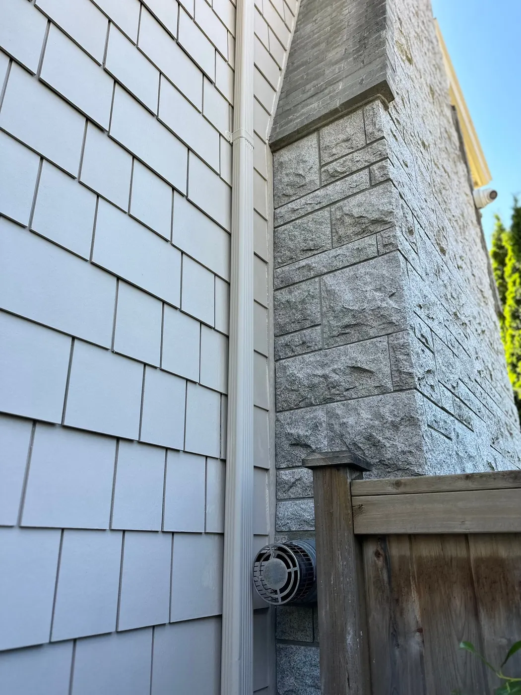 Pale grey shingle siding, white downspout and a stone chimney on a Vancouver, BC home exterior.