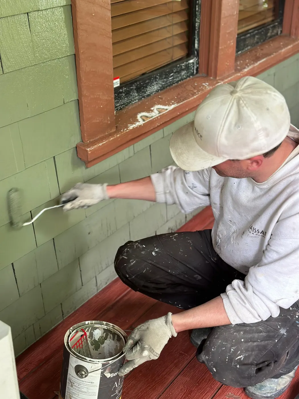 Painter rolling fresh sage green paint onto cedar shingle siding on a Vancouver home exterior