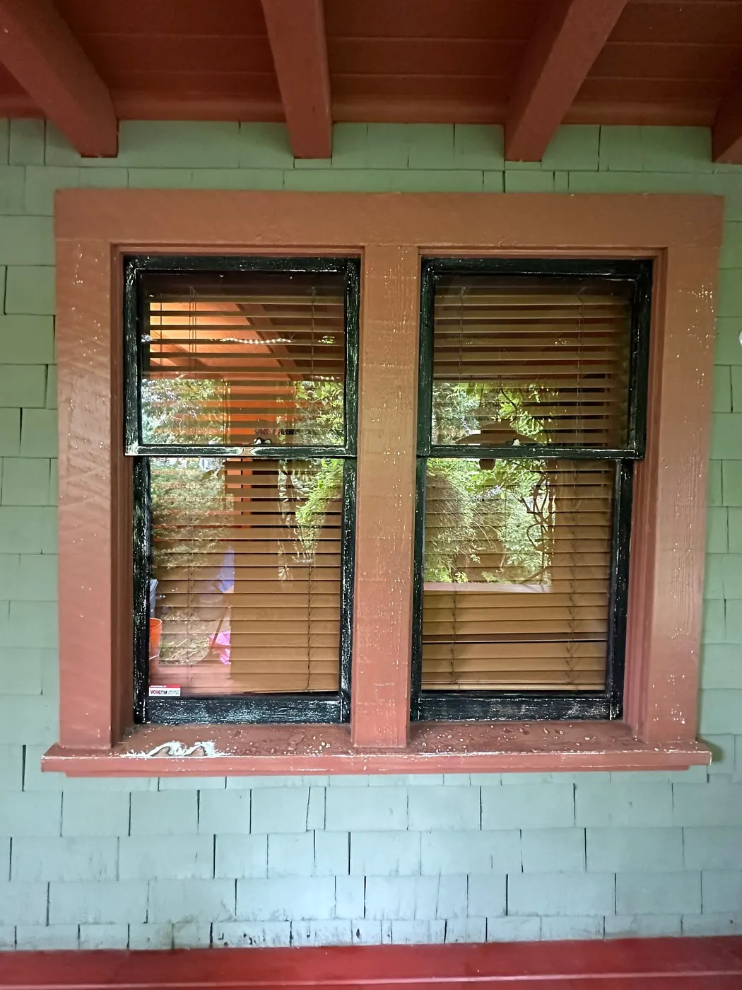 Freshly painted double-hung window with sage green siding and terracotta trim on a Vancouver home