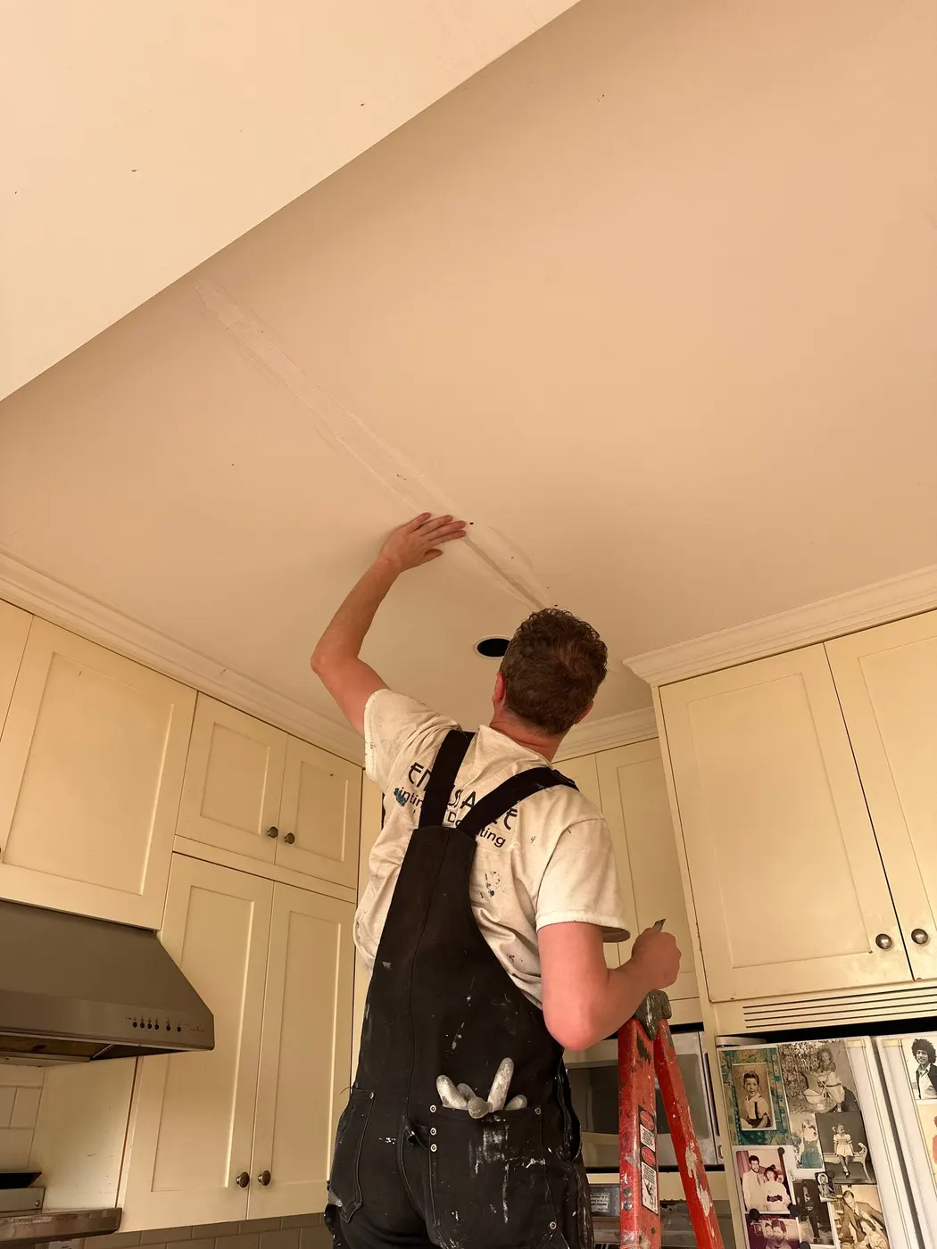 Painter smoothing a taped ceiling crack repair in a Vancouver kitchen before applying finish paint.