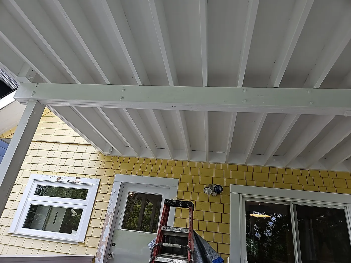 Freshly painted white deck ceiling and yellow shingle siding on a Vancouver home after repair