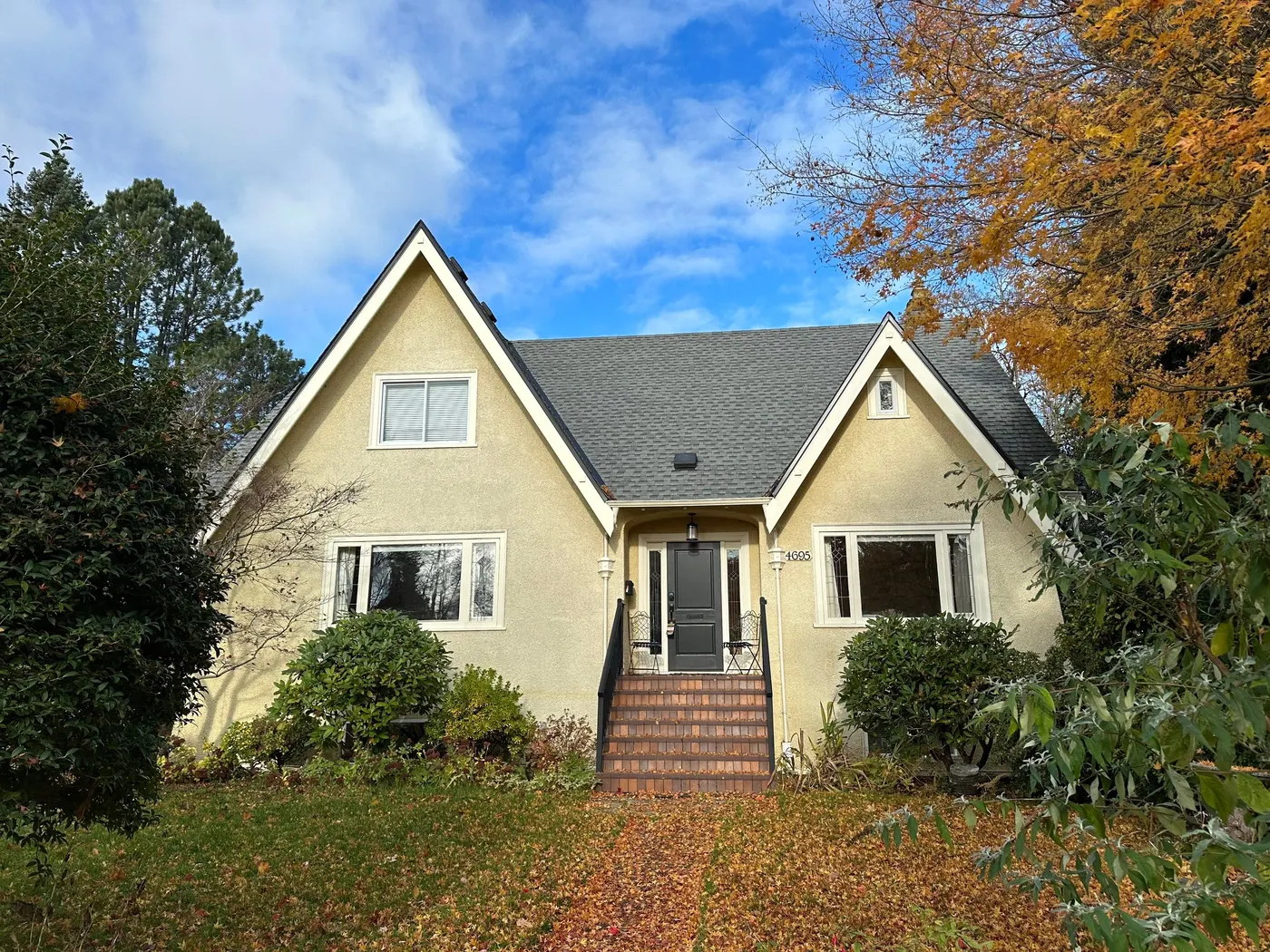 Cream stucco Tudor-style cottage exterior with a steep gray roof, painted by Renaissance Painting in Vancouver, BC.