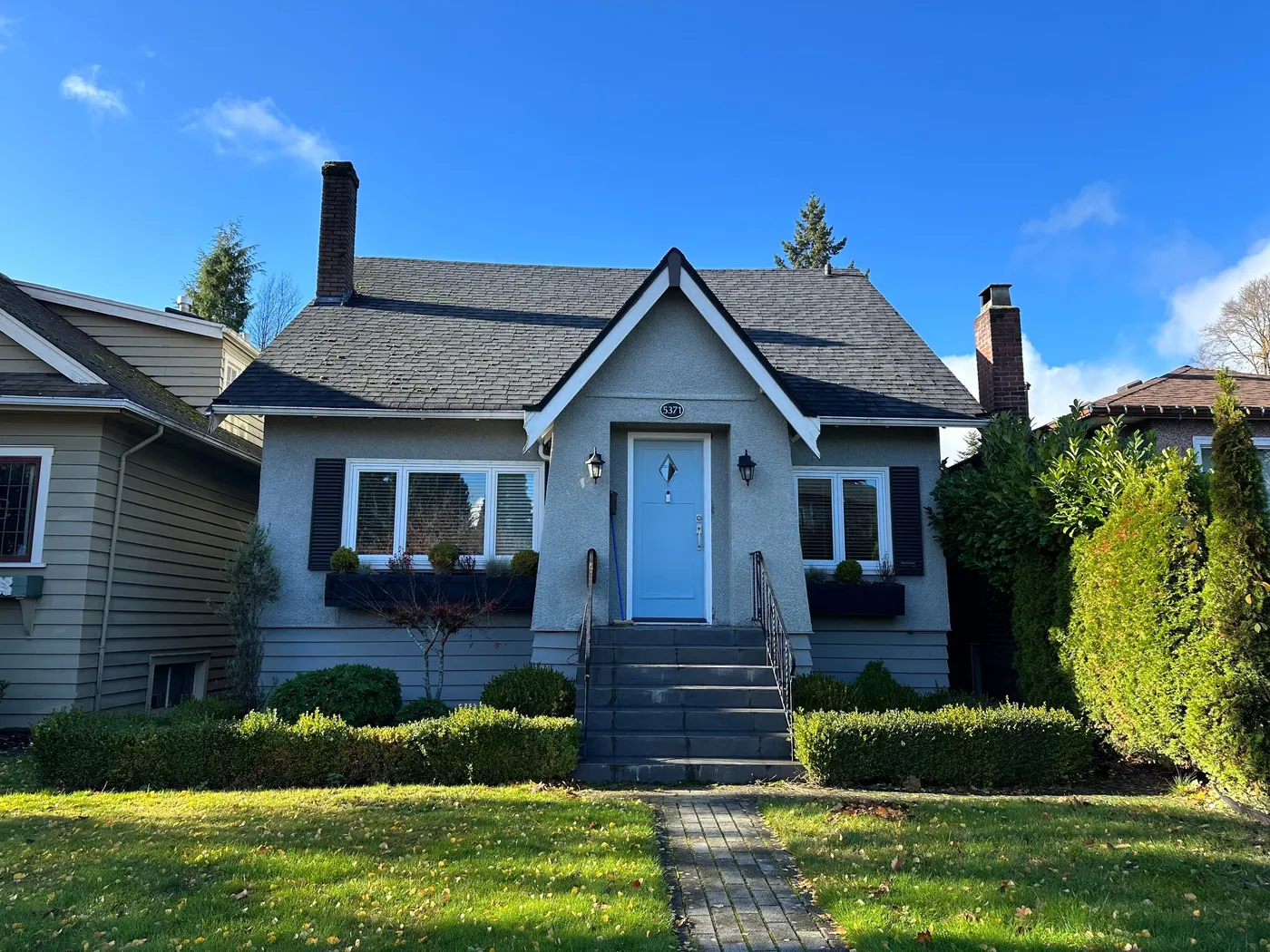 White stucco cottage exterior with a light blue front door, painted by Renaissance Painting in Vancouver, BC.