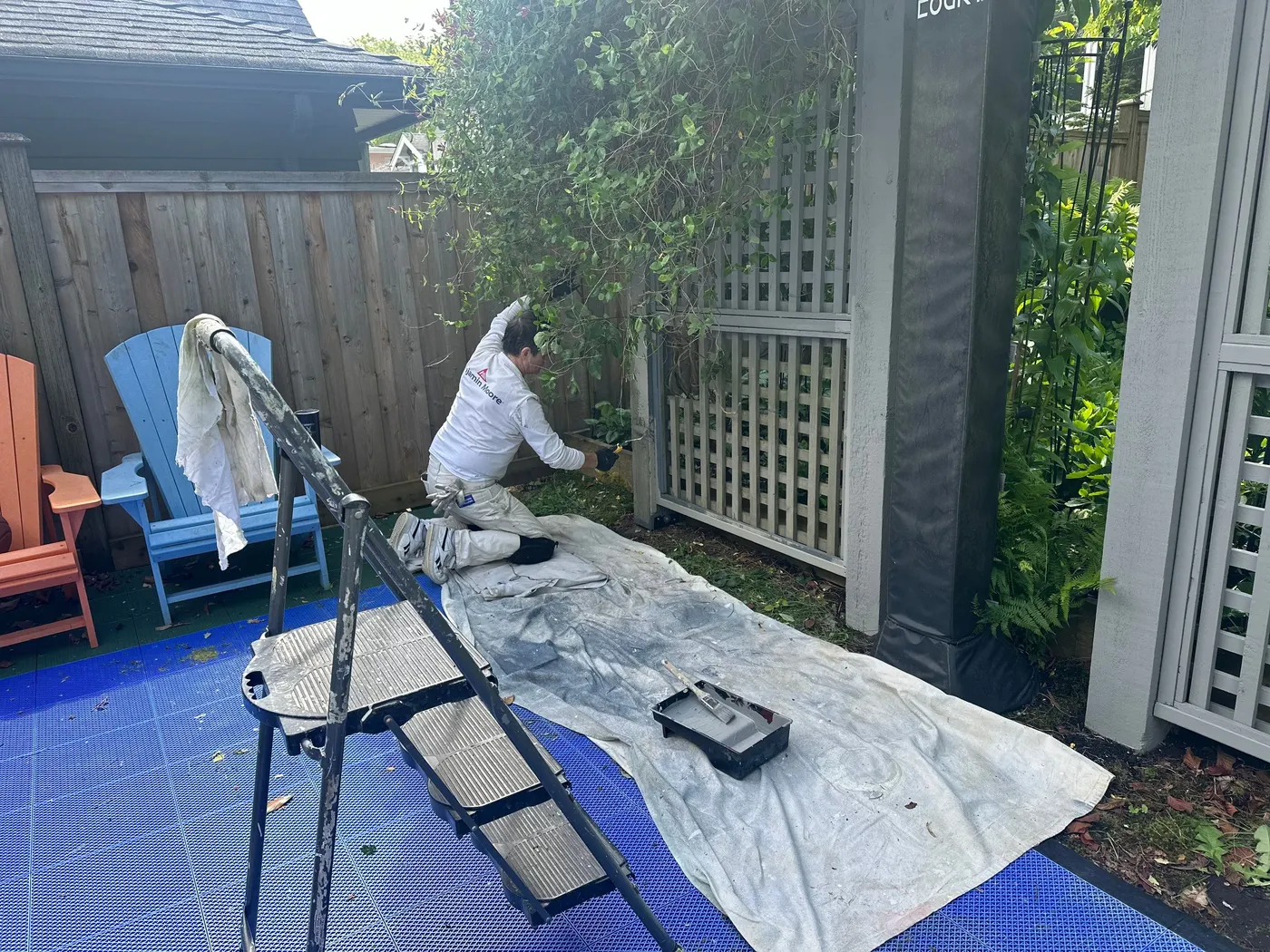 Painter applying paint to a wood gate post beside a garden lattice trellis in Vancouver