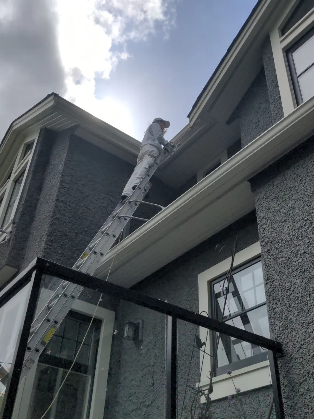 Painter on extension ladder brush-painting exterior fascia and eaves on a Kinahan Vancouver home