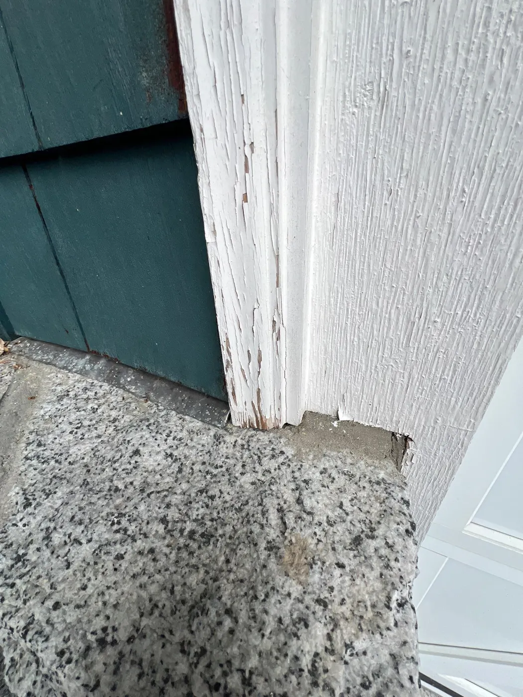 Peeling paint at the base of a wood porch post meeting a granite foundation on a Vancouver, BC house