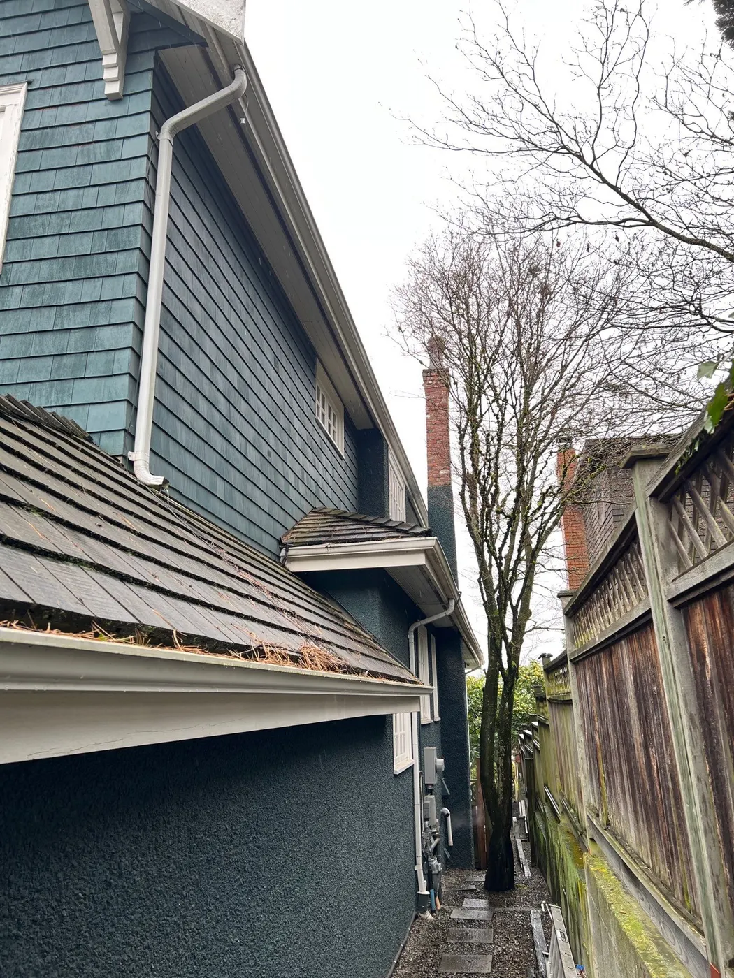 Side exterior view of a blue-green shingled Vancouver, BC home with a brick chimney and narrow side path