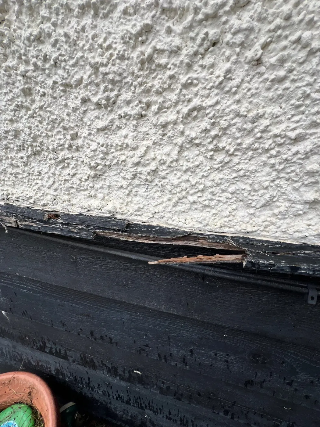Rotted black fascia board along a stucco roofline, flagged for carpentry repair in Vancouver, BC.