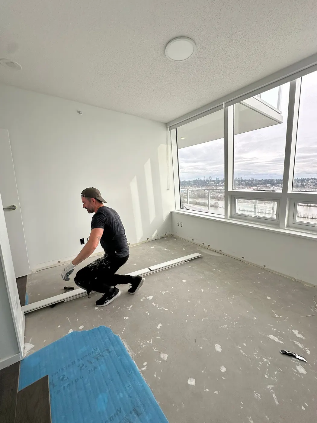 Painter installing baseboard trim in a high-rise condo with a river view in Metro Vancouver, BC