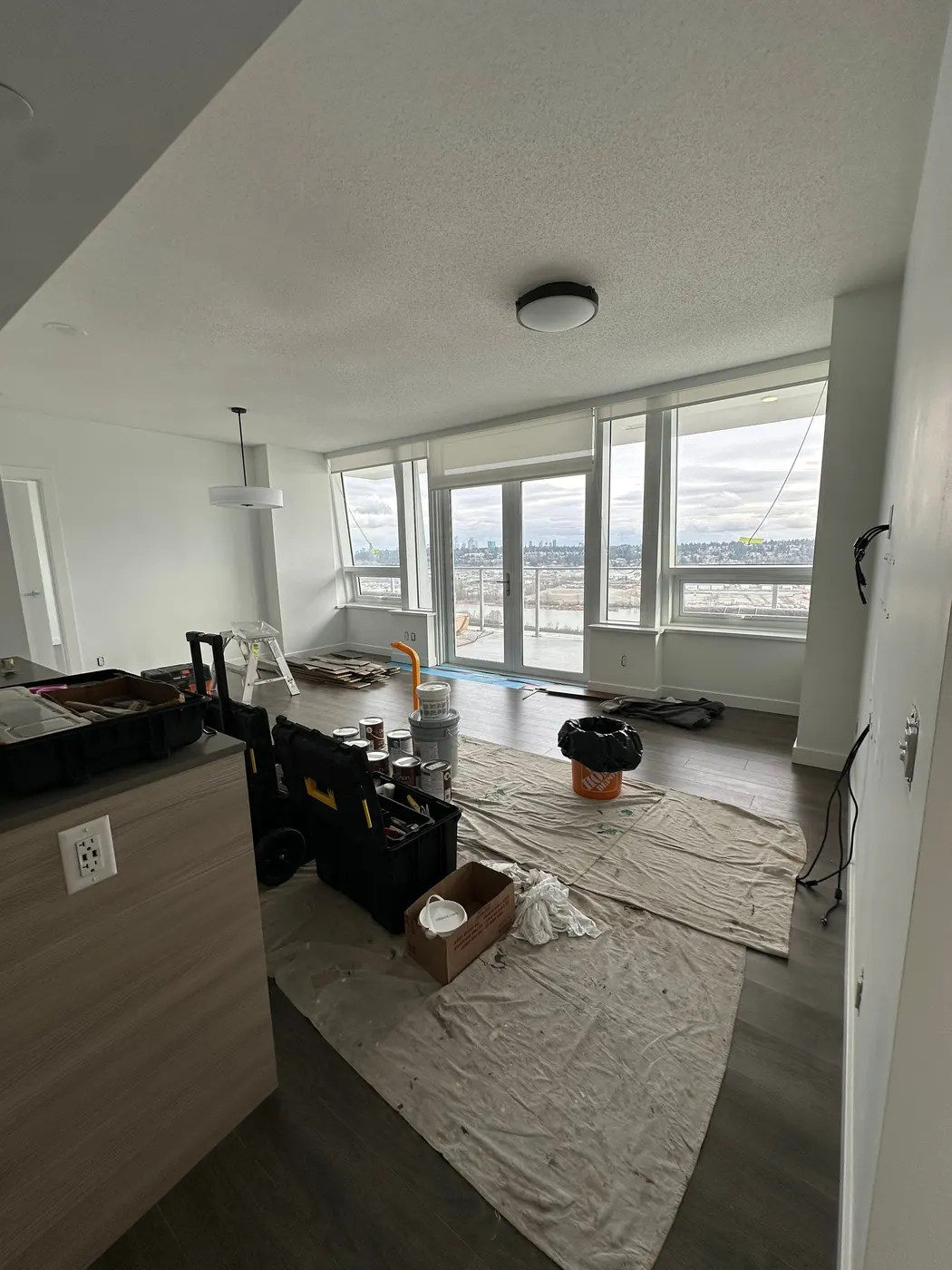 Living room set up with paint cans and drop cloths for a condo painting project in Metro Vancouver