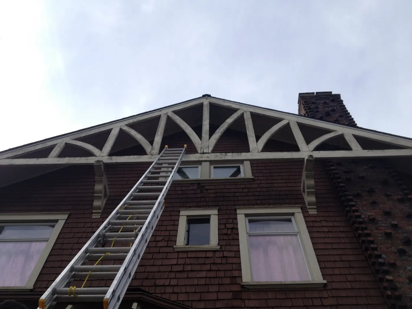 Gable roofline and chimney of a Vancouver, BC home with a ladder set up for exterior carpentry access