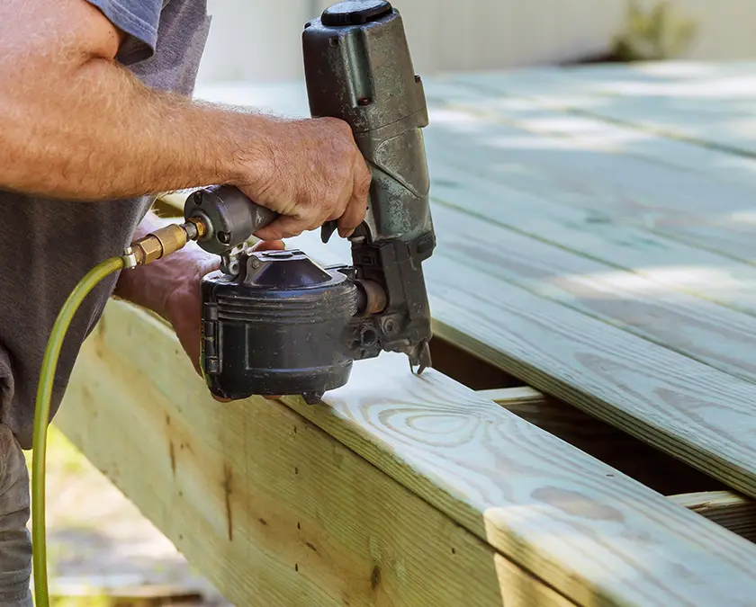 Man finishing off a deck with a nail gun.