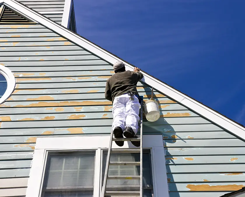 Man repairing siding from ladder before painting.