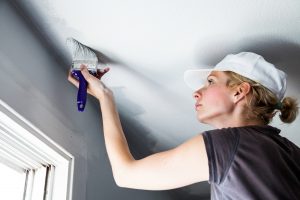 Woman painting the edges of the ceiling with a paintbrush.
