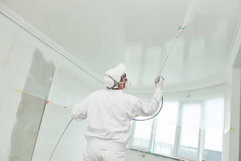 The painting contractor is spray painting a celling in a white colour.