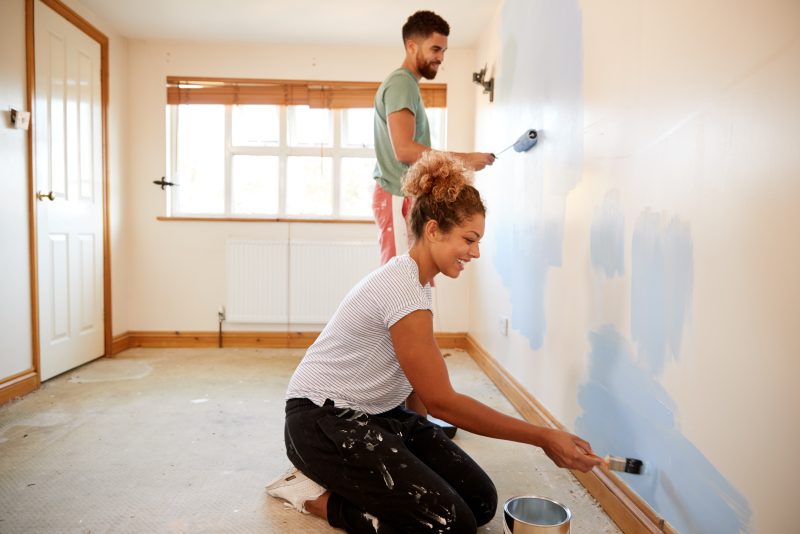 A happy couple is painting a white wall in a blue colour.