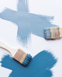 Two paintbrushes applying vibrant blue latex paint strokes on a white surface, showcasing the smooth application and rich color of the paint.