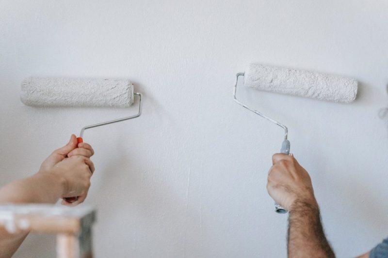2 contractors are painting interior wall in white with 2 painting rollers.