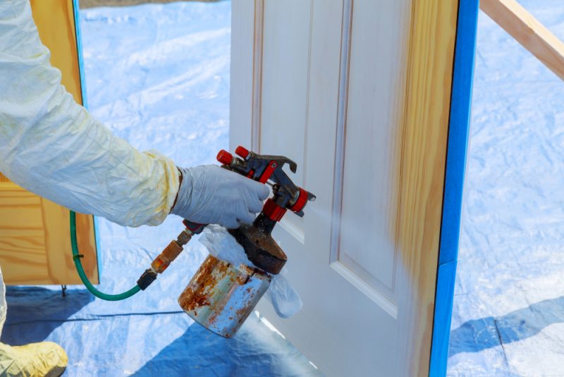 A spray painting professional is spray painting a door in white colour.