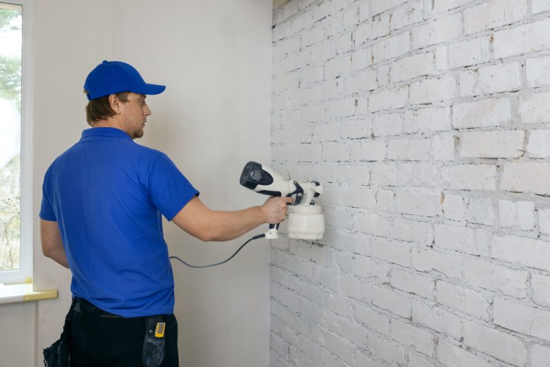 Professional home interior painter is spray painting a brick wall