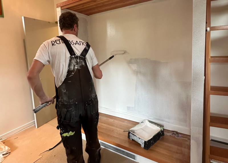 A contractor painting a wall in a white colour with a roller and a paint tray.