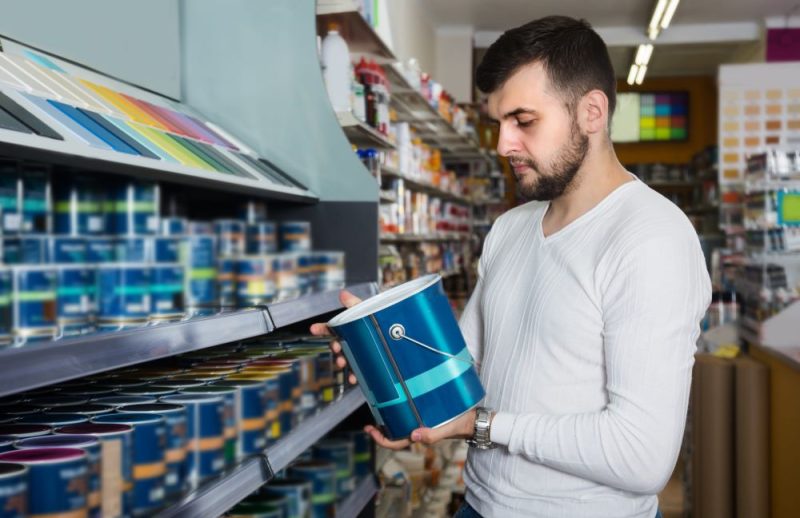 A man choosing paint in a store and looking on a blue paint can.