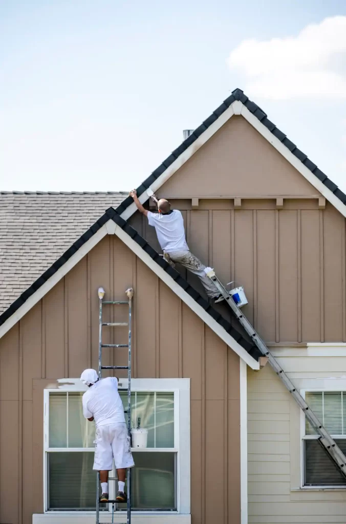 2 painters are painting house top part.