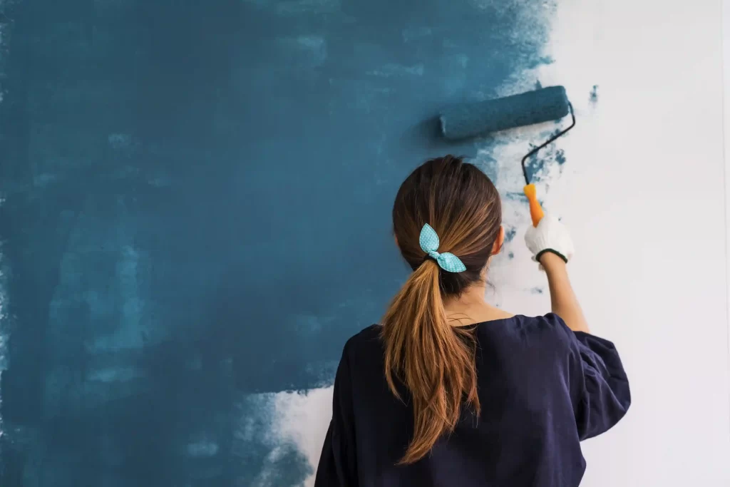 A woman painter is painting a white wall into a blue colour.