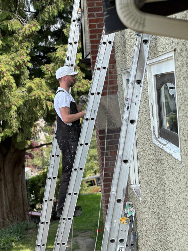a painter is painting a stucco exterior wall on a ladder.