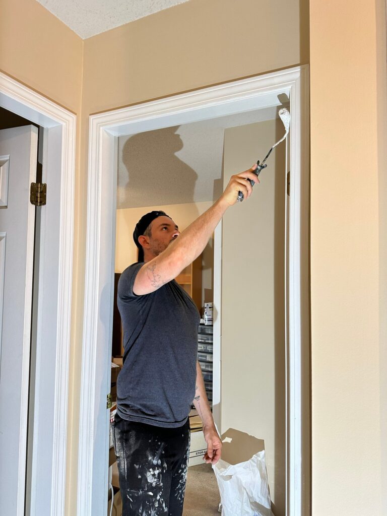 A painter in a dark gray t-shirt is painting a door in a white colour.