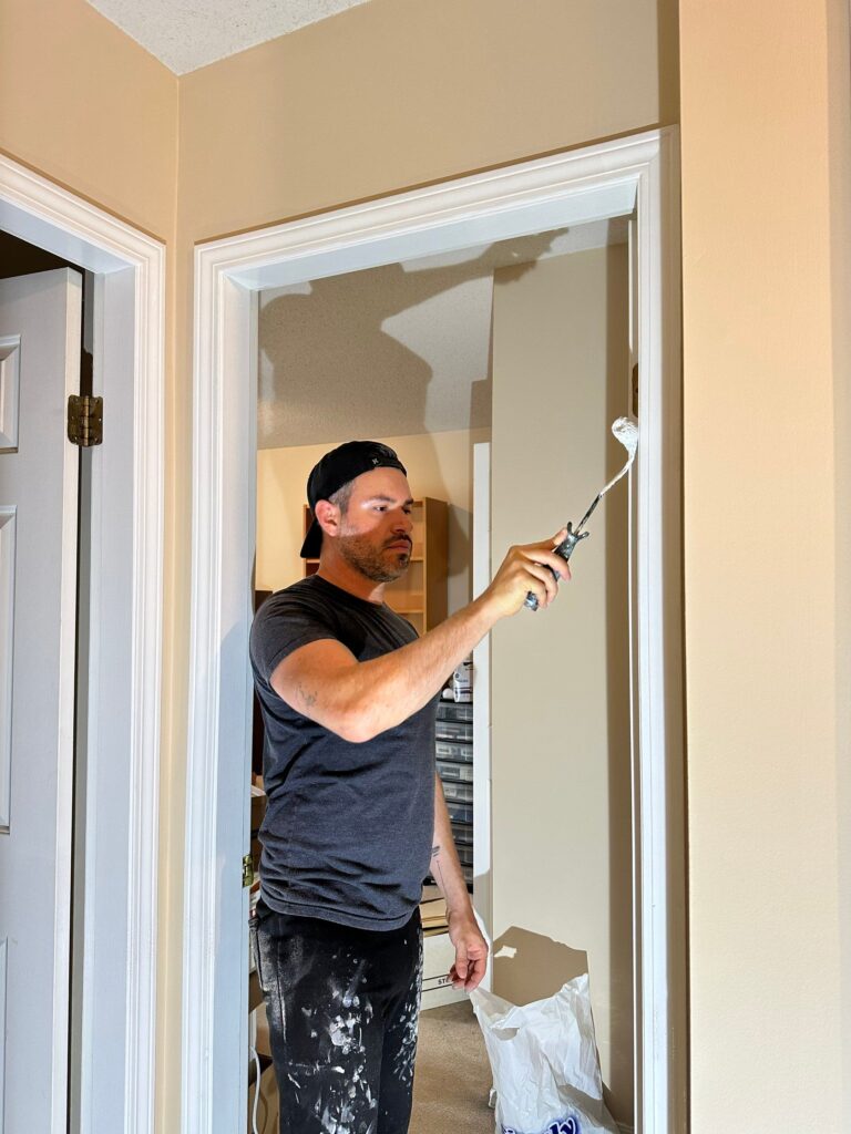 A painter in a dark gray t-shirt is painting a door in a white colour. 