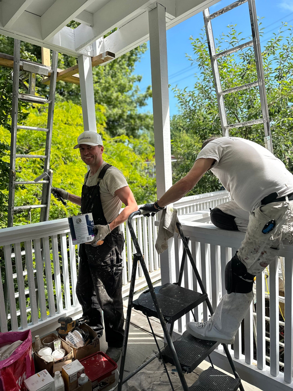 A couple of painter are painting a railing in a white colour with a painting materials in the middle.