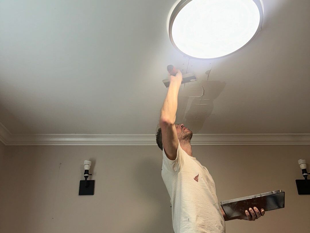 Worker applying joint compound to ceiling after popcorn texture removal—part of interior ceiling resurfacing and refinishing process.