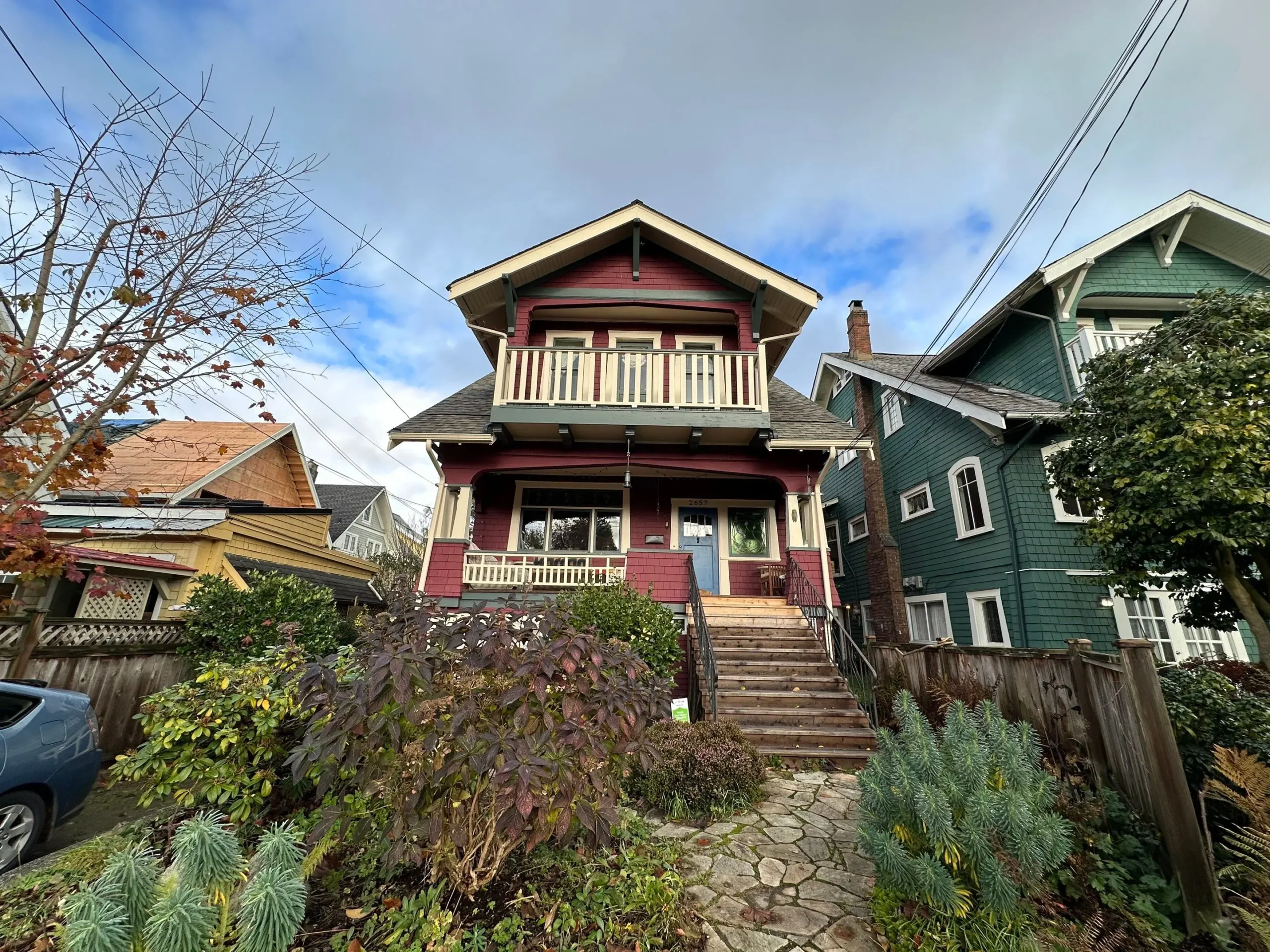 Two-storey Craftsman-style house with red siding, white trim, and a front garden pathway in a Vancouver neighbourhood.