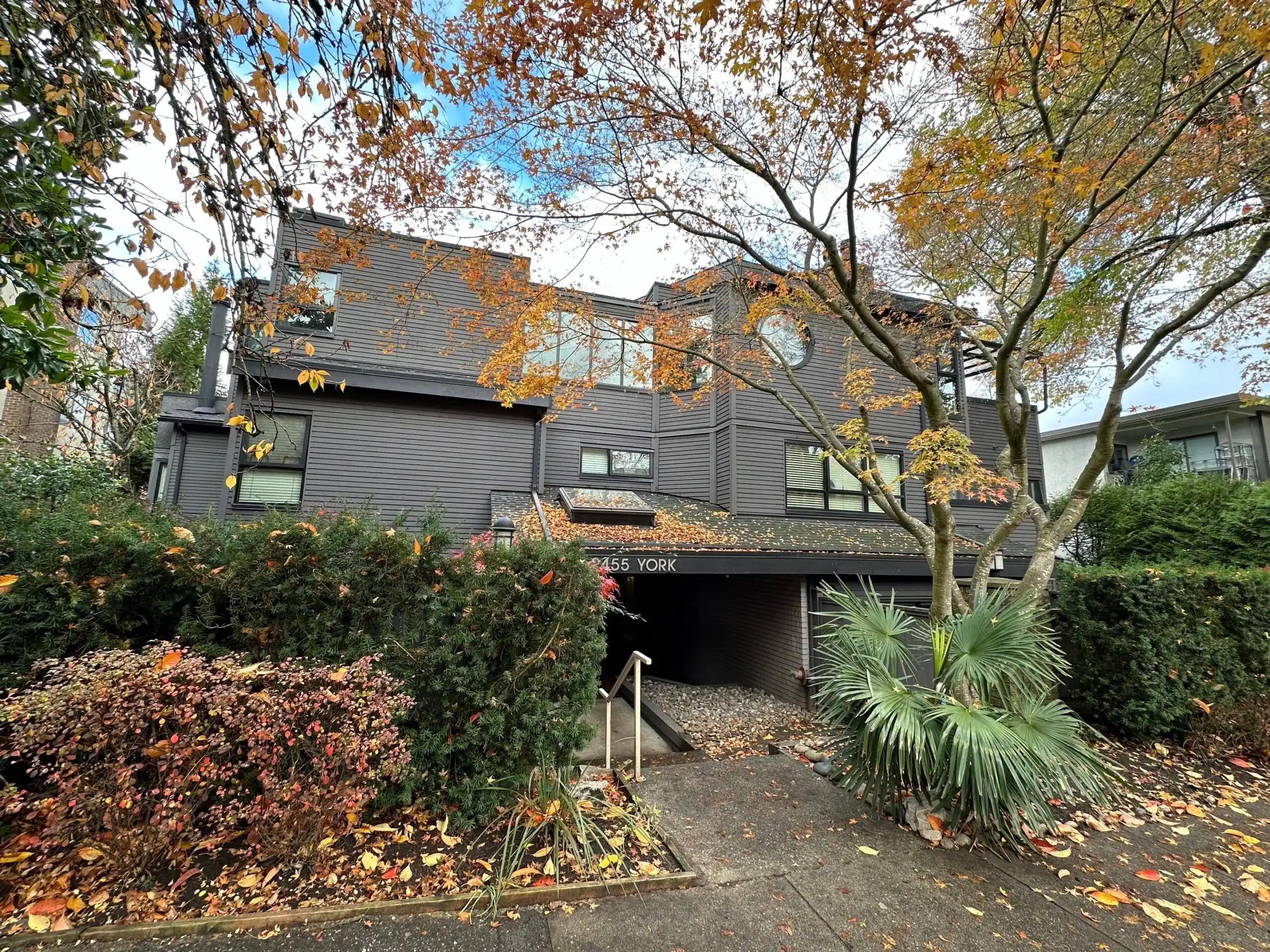 Fresh, professional exterior painting on a modern building in Vancouver shown with clean dark siding framed by fall foliage.