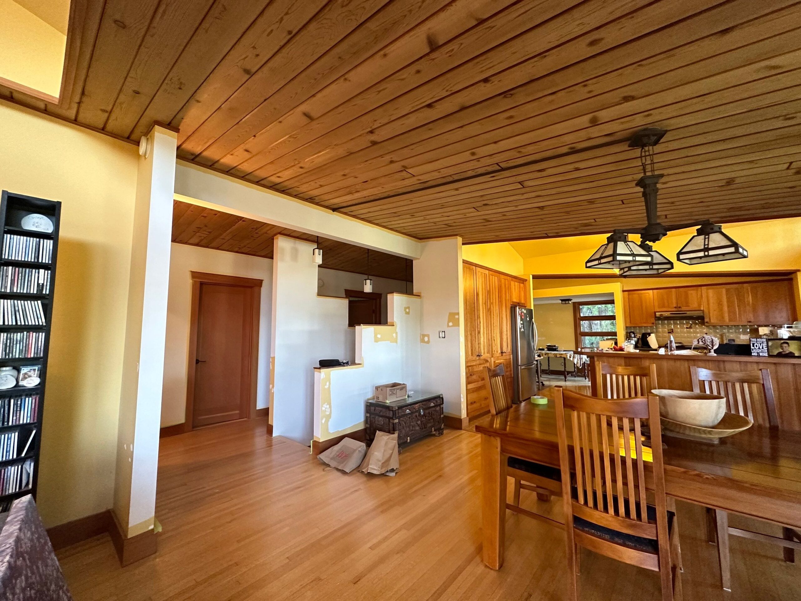 Open-plan kitchen and dining area with wood ceiling, yellow walls, and hardwood floors in a warm rustic interior.