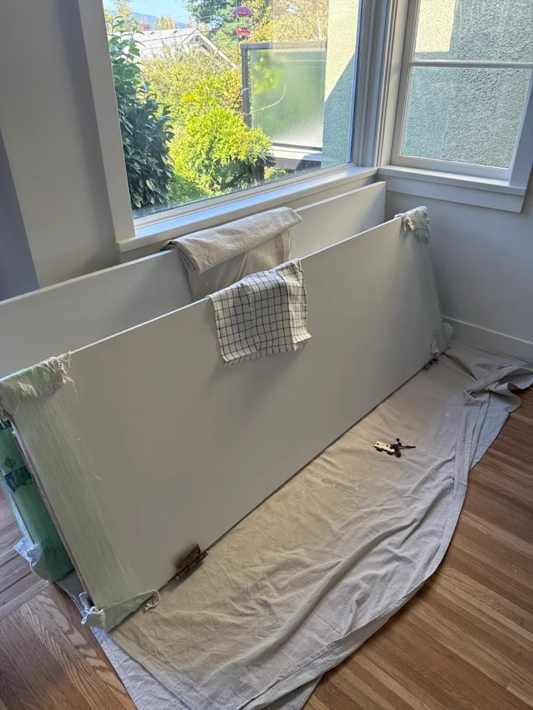 Interior door painting setup with removed doors drying on cloth near window during home renovation