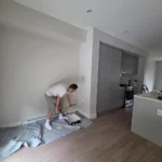 Contractor painting living room wall in modern interior renovation with open kitchen layout