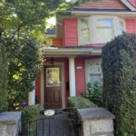 Pink Victorian-style home entry with gated walkway, front porch columns, and landscaped greenery