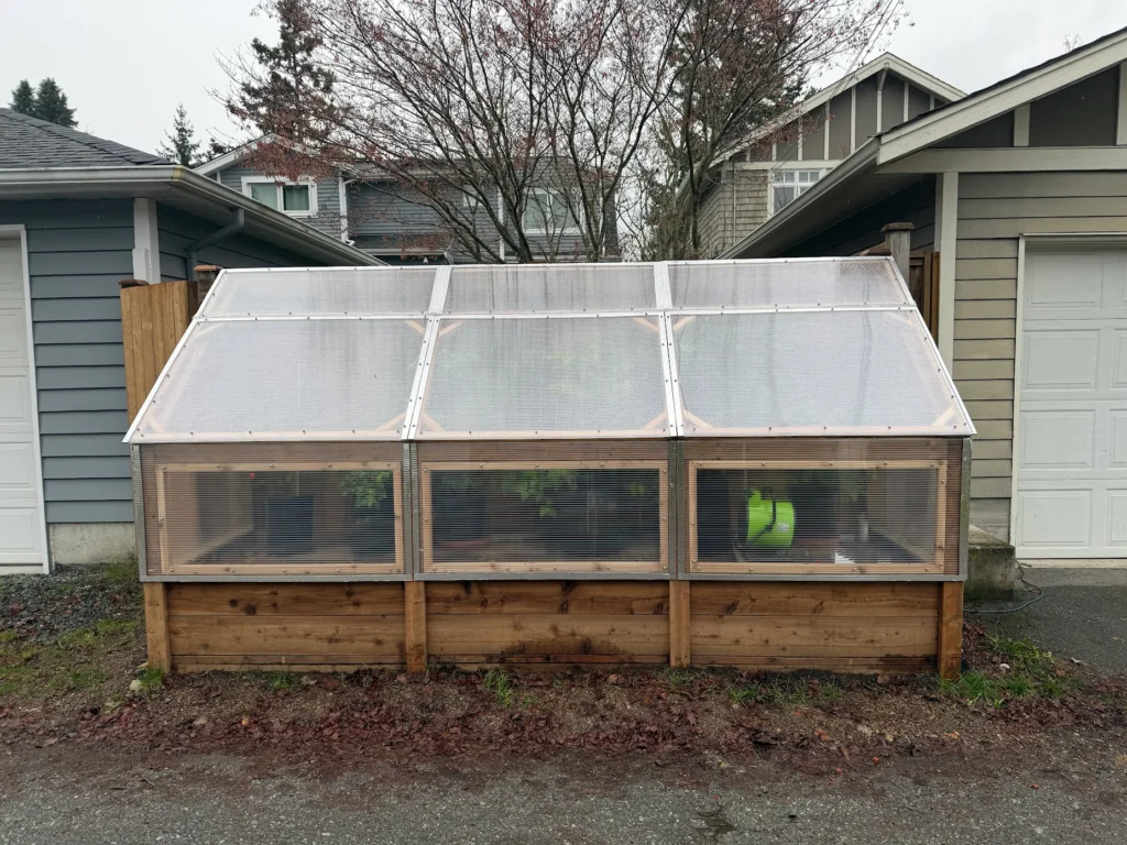 Backyard cold frame greenhouse with wood base, clear polycarbonate panels, and raised garden beds