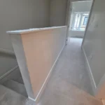 Upstairs hallway with carpet flooring, half wall railing, and doorway during modern interior renovation