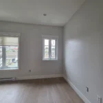 Empty bedroom with light wood floors, white walls, and large windows in modern interior renovation