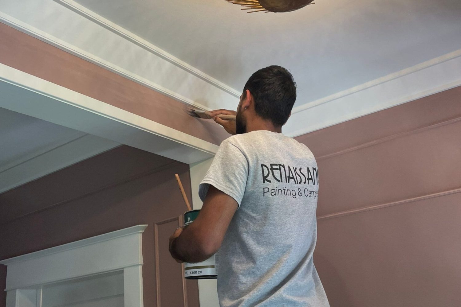 Worker painting ceiling with crown molding using a roller, professional finishing