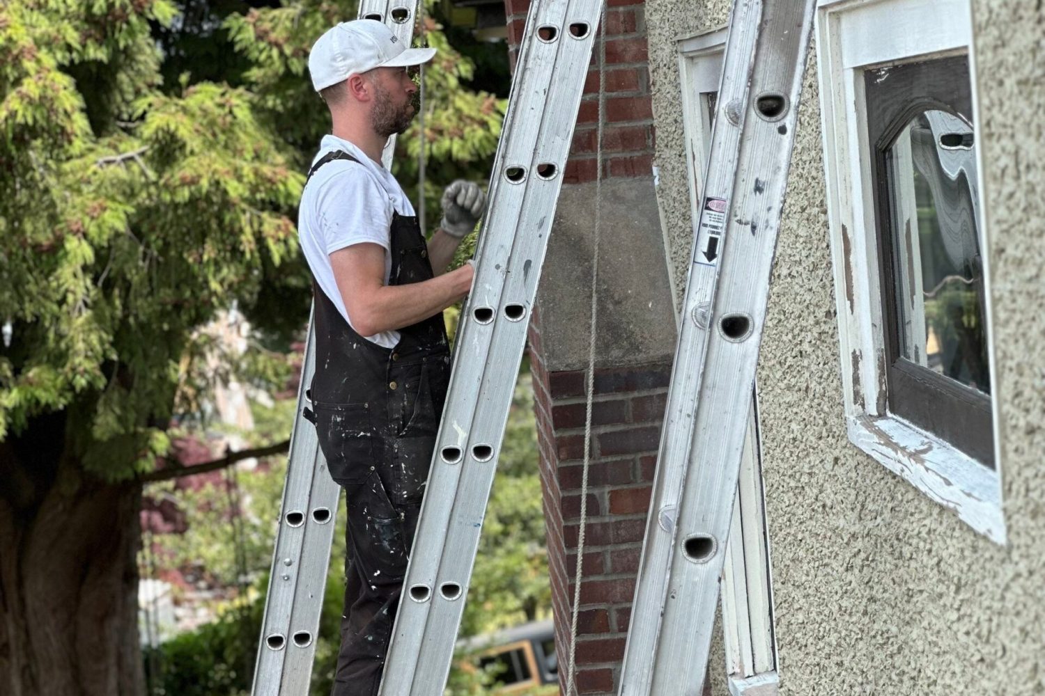 Painting contractor is doing exterior stucco painting on a ladder.